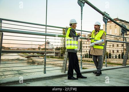 Two senior construction managers are standing on the bridge while talking and smiling Stock Photo