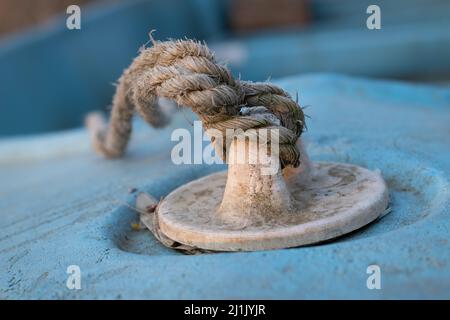 Rope knot on bow of old boat with cracked blue paint ashore in selective focus Stock Photo