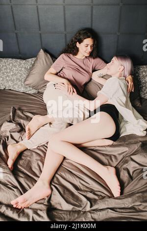 Happy attractive young Caucasian lesbians in sleepwear looking at rach other while waking up together Stock Photo