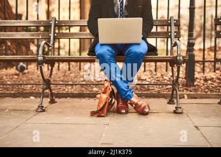 When the office isnt enough. Shot of an unrecognizable man working on his laptop while being seated on a bench outside during the day. Stock Photo