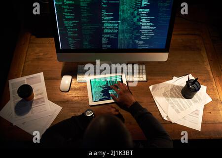 Coding on multiple platforms. High angle shot of an unrecognizable man coding on his tablet in the office. Stock Photo