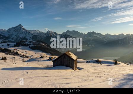 Snow-covered mountain meadows with hay huts in front of the panorama of the Glarus Alps at sunset, Canton Sankt Gallen, Switzerland Stock Photo