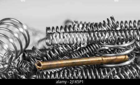 Unique golden rusty tension coil spring in heap of silvery compression springs on white background. Closeup of helical elastic wire steel machine part. Stock Photo