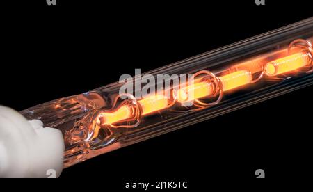 Glowing coiled resistance wire inside heating element on black background. Closeup of orange hot metal conductor in laser printer finisher glass tube. Stock Photo