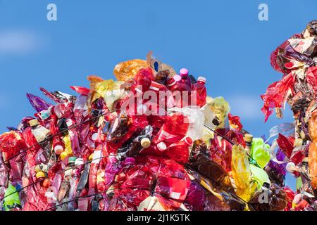 Detail of red plastic waste compressed in bale on trash landfill with blue sky background. Close-up of used crumpled PET bottles on dump. Eco problem. Stock Photo