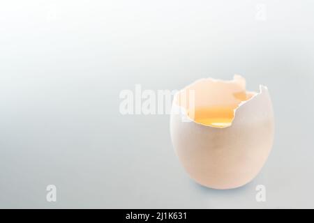 Cracked white egg with yellow yolk on a light gray background, copy space, selected soft focus, very narrow depth of field Stock Photo