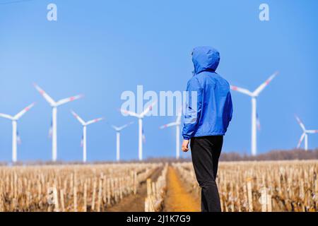 Man engineer looking on the wind turbines through the vineyard. Concept of rural alternative energy. Stock Photo