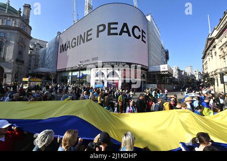 26/03/2022. London, UK.  People walk past the Piccadilly Lights displaying Yoko Ono’s ‘IMAGINE PEACE’ artwork, taking part in a solidarity march ‘London Stands with Ukraine’ sending a unified message in. Sport of Ukrainian people during the current invasion of the country by Russia. The artwork was commissioned by CIRCA in collaboration with Serpentine Gallery.. Photo by Ray Tang. Stock Photo