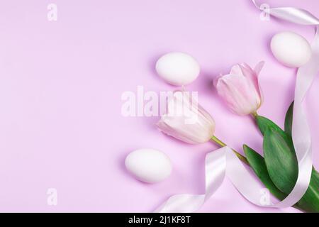 Easter holiday background with white chicken eggs and pink tulip flowers on pink background. Congratulatory Easter background with copy space. Stock Photo