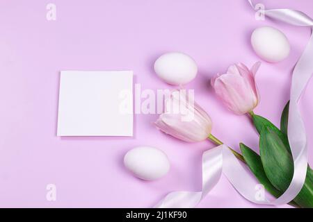 Easter greeting card with white eggs and pink tulip flowers over pink background. Top view flat lay with image copy space. Stock Photo