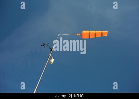 Orange conical windsock and wind cone - meteorologic device and tool on pole and post. Measuring and indicating wind during windy weather. Blue sky. Stock Photo