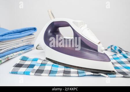 Iron on the ironing board and plaid children's shirt on a white background. Care of children's clothing Stock Photo