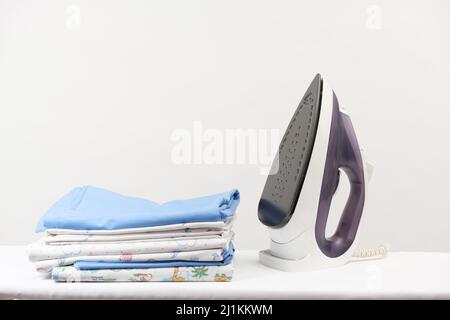 Iron and a stack of ironed clothes and baby diapers on a white background with space for text. Stock Photo
