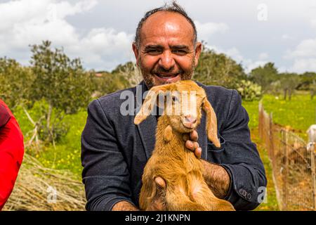 Farmer in North Cyprus with small Aleppo goat. The goat has distinctive long ears. In North Cyprus it is bred for its high milk yield. In the village of Akdeniz, which translated means Mediterranean Sea, you get an impression of typical Cypriot country life. Mayor Tarik shows the goats which are only one day old
