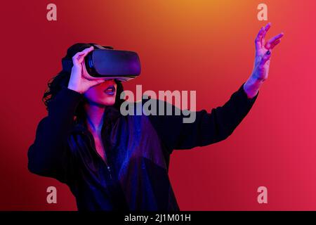 Young woman is using the headset for virtual reality. Portrait of modern woman with trendy look and bright colors. Stock Photo
