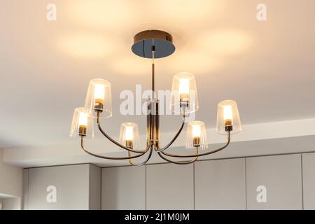 Chandelier hanging from the ceiling with lights on Stock Photo