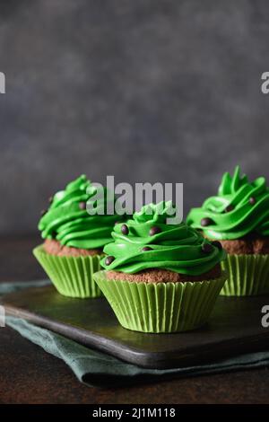 Tasty homemade chocolates cupcake with green whipped cream on brown background. Vertical format. Close up. Stock Photo