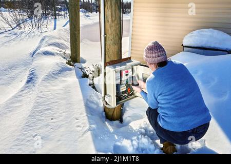 Outdoor electrical panel with an electric meter in countryside in winter, woman takes readings and calculates consumption of electricity using Stock Photo