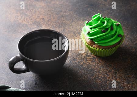 St. Patrick's Day coffee and chocolate cupcake with green whipped cream on brown background. Close up. Stock Photo