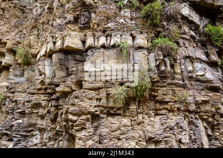 Low angle of uneven rocky cliff covered with patches of green grass on summer day in countryside Stock Photo