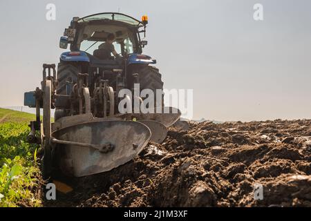 Reenascreena, West Cork, Ireland. 26th Mar, 2022. Reenascreena based farmer, Cian Daly who is in partnership with his grandfather Michael, ploughs a field to plant wheat on a warm, sunny day in West Cork. Cian and Michael farm beef and dairy on 160 acres and Cian was using a New Holland T6050 tractor and Fiskars 5 furrow plough to prepare the field for planting. Credit: AG News/Alamy Live News Stock Photo