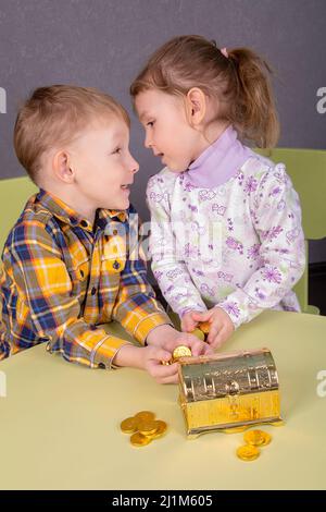 a boy and a girl hold treasures from a golden chest in the form of chocolate coins in their palms Stock Photo