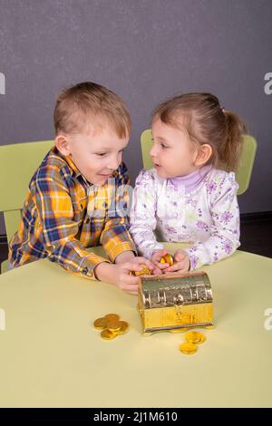 a boy and a girl hold treasures from a golden chest in the form of chocolate coins in their palms Stock Photo