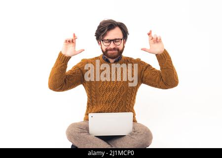 Young handsome Caucasian man with glasses keeping his hands up and having fingers crossed, eyes closed brown knitted sweater medium shot isolated white background . High quality photo Stock Photo