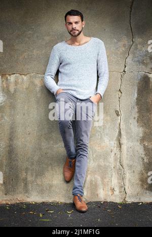 Casual urban style is his signature look. Shot of a handsome young man posing against an urban wall. Stock Photo