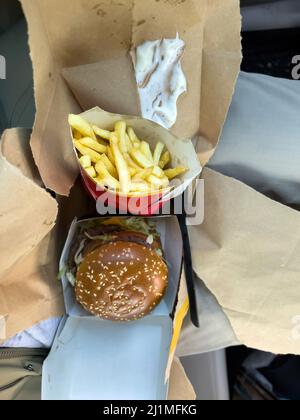 Basel, Switzerland - Dec 20, 2021: View from above on the knees of delicious French fries and triple burger bought from McDonalds Basel restaurant Stock Photo