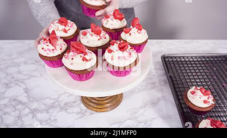 Step by step. Arranging red velvet cupcakes on a marble cake stand. Stock Photo