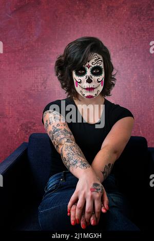 Tattooed woman, brunette, facing the camera, with La Katrina makeup and with a spot of light on her face. Stock Photo