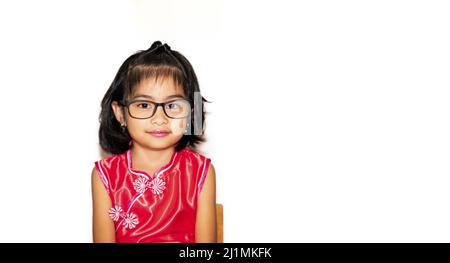 picture of beautiful liitle girl in red chinese dress wearing eye glasses sitting on chair Stock Photo