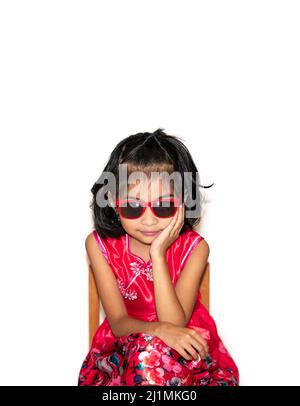 picture of beautiful liitle girl in red dress wearing sun glasses sitting on chair Stock Photo