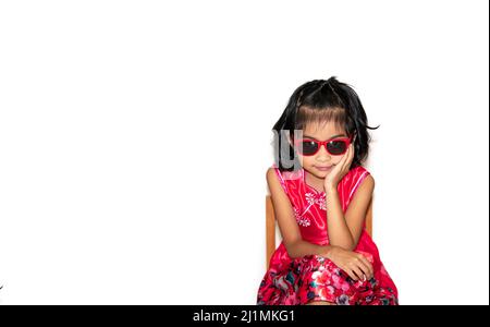picture of beautiful liitle girl in red dress wearing sun glasses sitting on chair Stock Photo