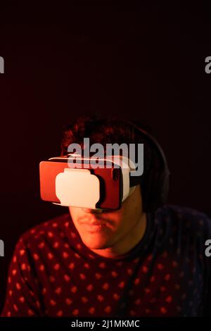 Young latin man using Virtual Reality VR Headset 3D Glasses. Dark backdrop. Low key. Copy space. Stock Photo