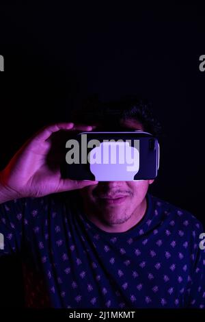 Young latin man using Virtual Reality VR Headset 3D Glasses. Dark backdrop. Low key. Copy space Stock Photo