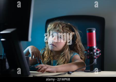 A little boy child uses a desktop at night, a child with computer screen in the room with neon lightning. Social network for kids. Stock Photo