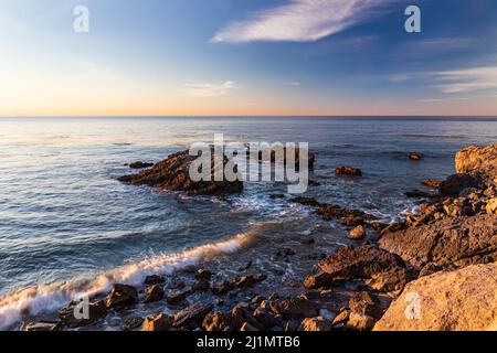 Rocky beach in Malibu, California in early morning. Calm Pacific ocean in the distance; blue sky and clouds overhead. Stock Photo