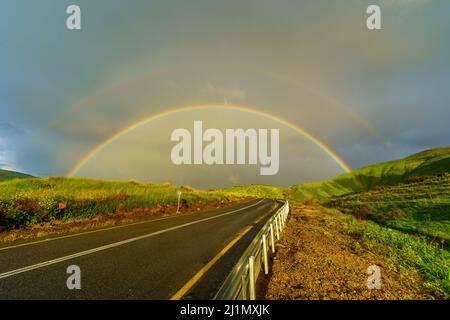 View of a double rainbow, on the slopes of the Golan Heights, with a trilingual mine warning sign, on a foggy winter day. Northern Israel Stock Photo