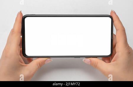 cell phone mockup in horizontal position. watching streaming video on phone. close up hands hold cellphone whith blank screen on gray background. Mobi Stock Photo