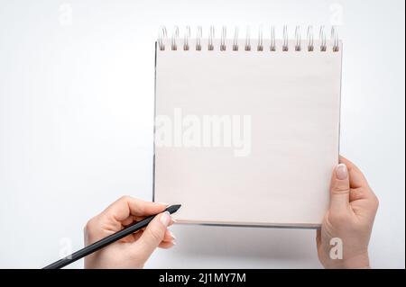 woman hands writing in empty notebook at white desk. Top view female hands with pencil writing on notebook notepad. copyspace. Woman lefty writing in Stock Photo