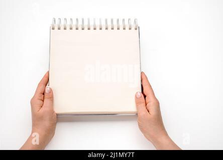 Notepad mockup. female hands holding blank spiral notepad or calendar over white table background. Hand holding an empty journal binder notepad or not Stock Photo