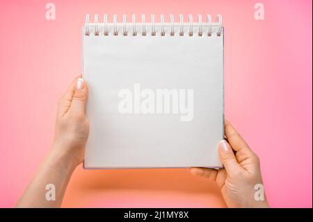 close up view female hands hold mockup notepad on pink purple background. Woman holding notepad. Mockup notepad with woman hands on pink table backgro Stock Photo