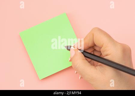 Hand written notes black pencil on green sticker. pink table background. woman hand writing on green sticky notes. Business people meeting and use not Stock Photo
