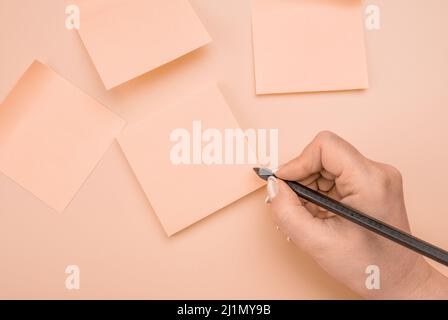 Hand written notes black pencil on sticker. pink pastel table background. woman hand writing on sticky notes. Business people meeting and use notes to Stock Photo