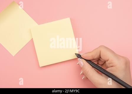woman hand writing on yellow sticky notes. Hand written notes black pencil on blank yellow sticker. pink table background. Business people meeting and Stock Photo