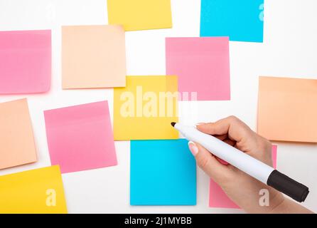 Mockup sticky Note Paper. Many colored empty sticker notes on white wall. hand with black marker ready to write. blank Sticker notes on white backgrou Stock Photo