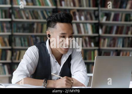 Smiling Korean guy sit in library studying online using laptop Stock Photo