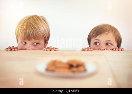 Who can resist a cookie. Two little boys sneakily trying to take a cookie from a plate. Stock Photo